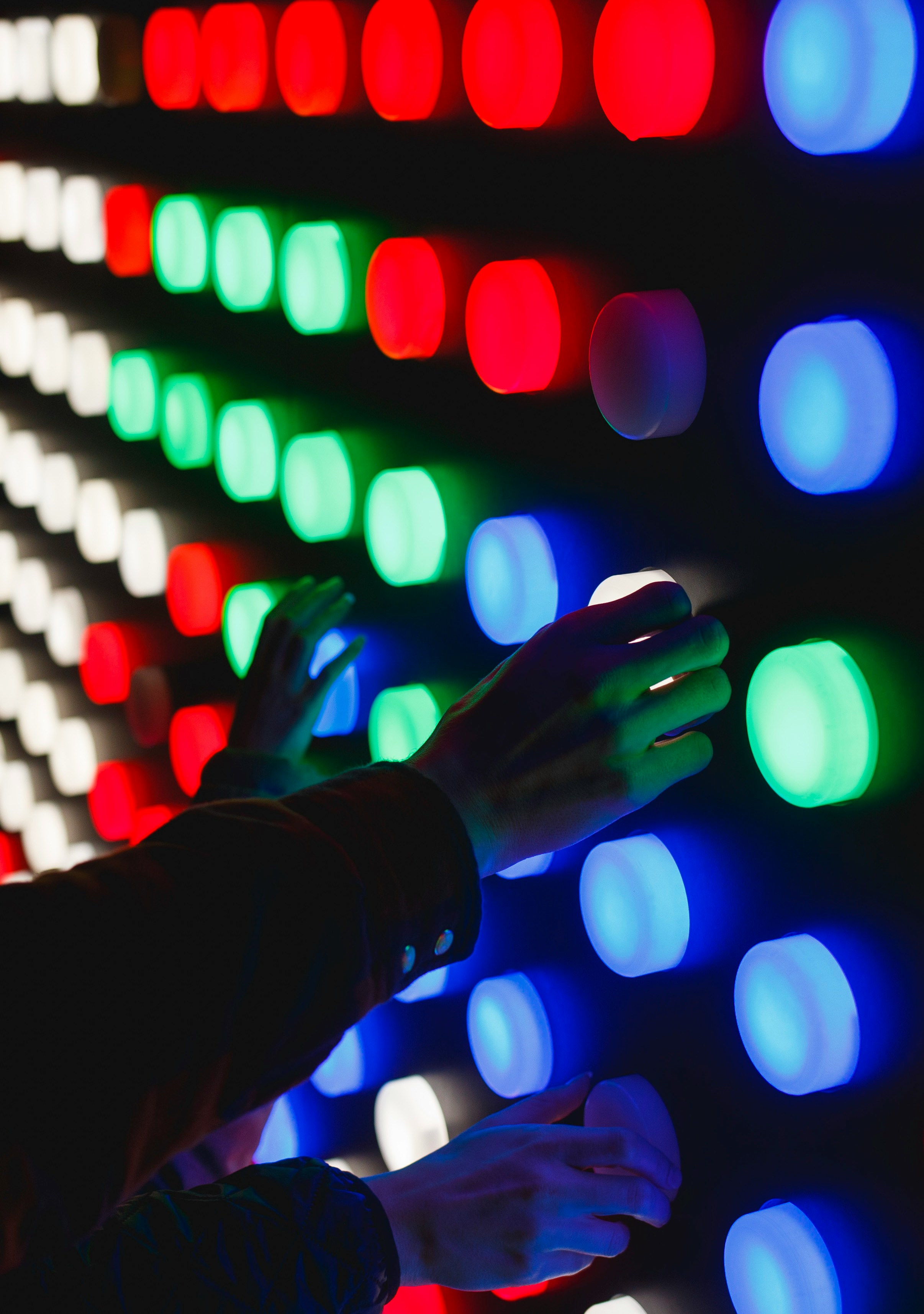 Person adjusting colorful illuminated pegs on a large interactive light pegboard.