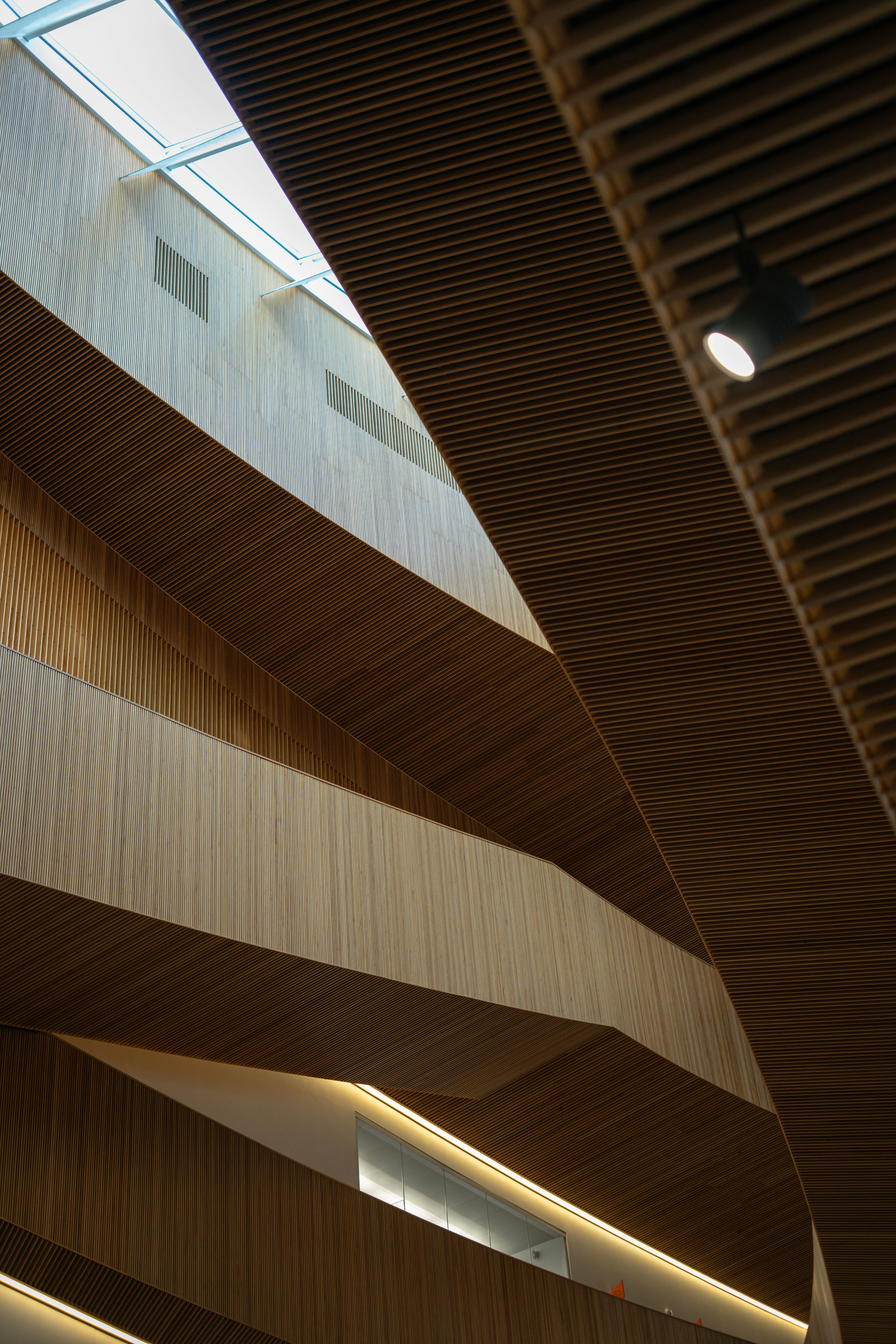 Interior view of a modern building ceiling with layered wooden slats and a skylight.