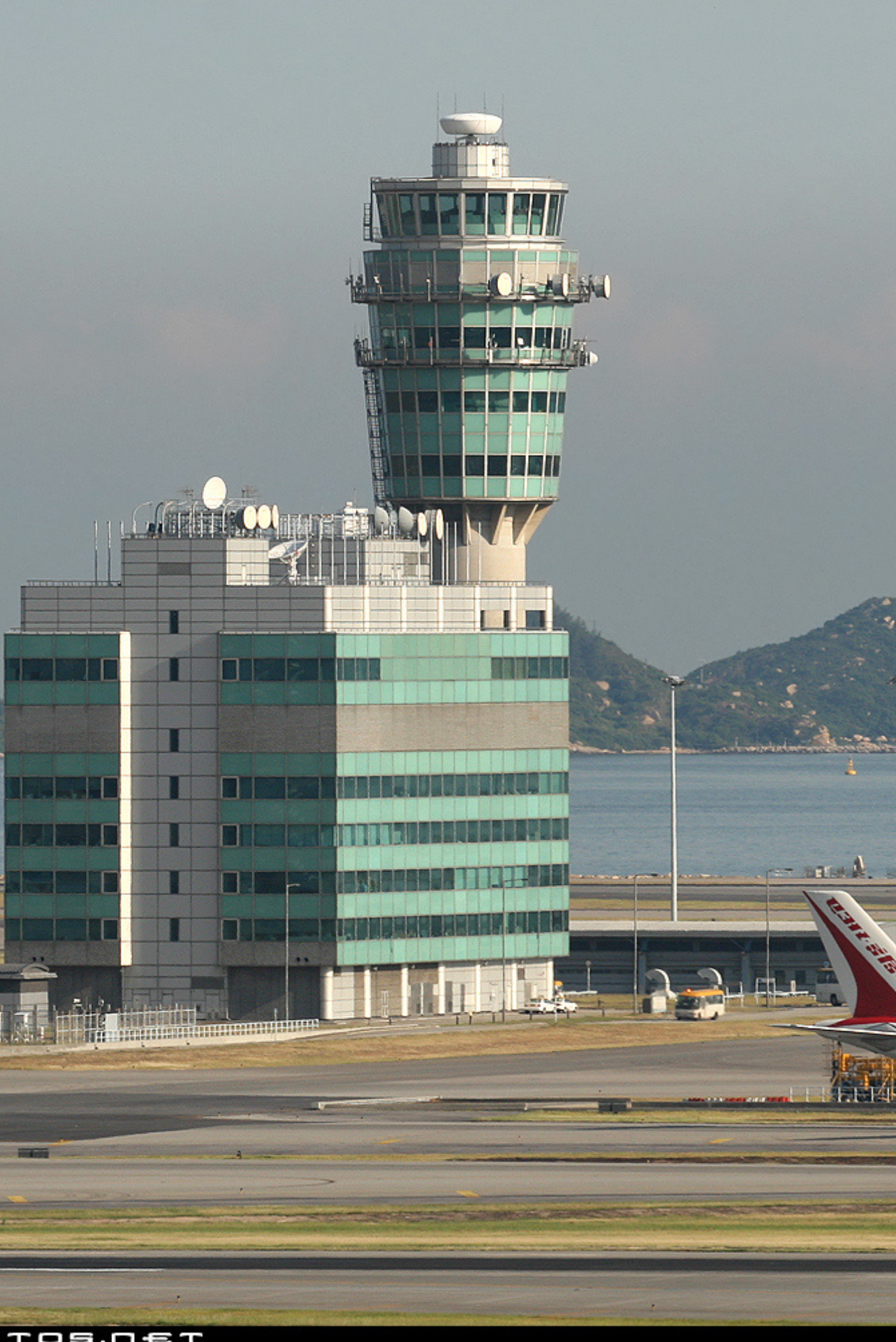 Airport control tower with a building base and mountainous coastline in the background.