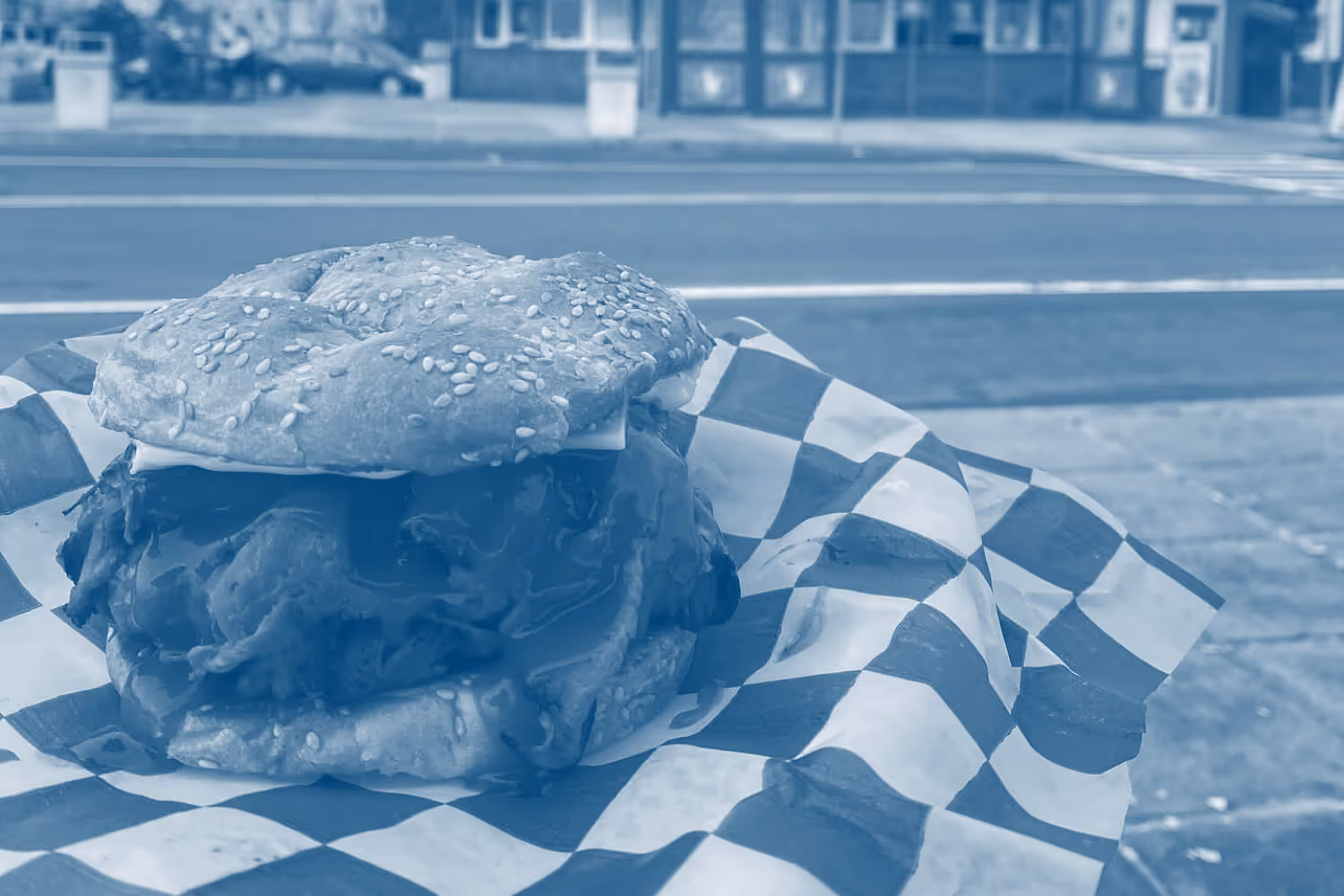 Pulled beef sandwich with melted cheese in a sesame seed bun on checkered paper.