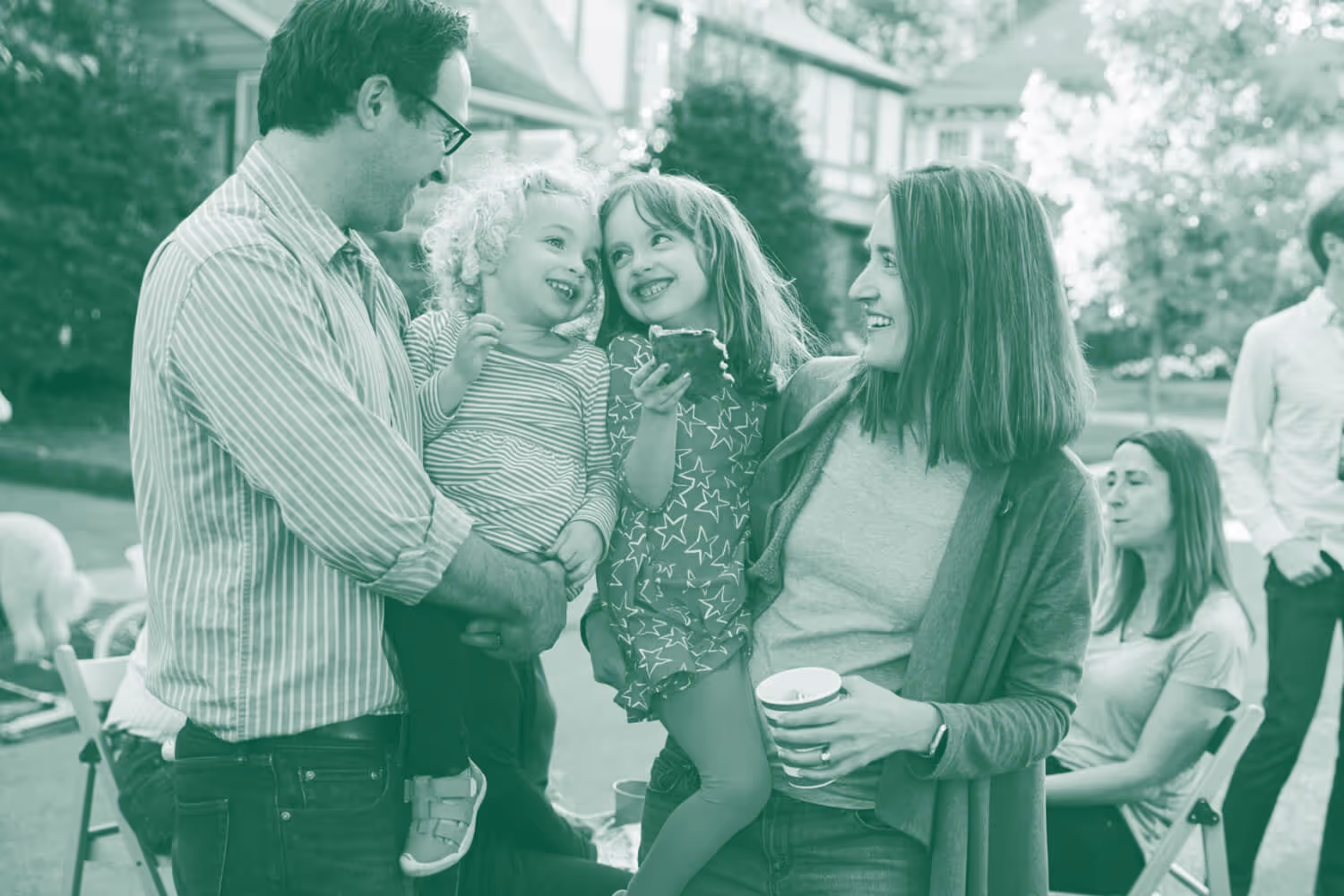 Smiling family of four at outdoor block party, with parents holding their two happy young children.