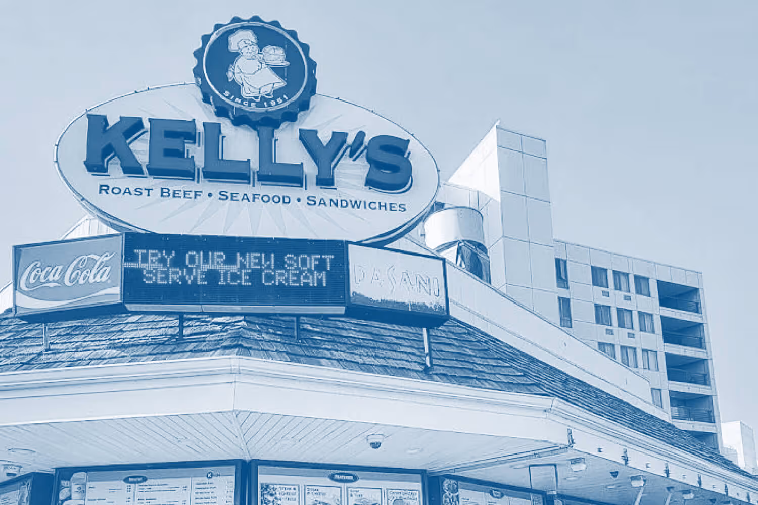 Exterior of Kelly's restaurant sign reading 'Roast Beef, Seafood, Sandwiches' with a digital board advertising soft-serve ice cream.