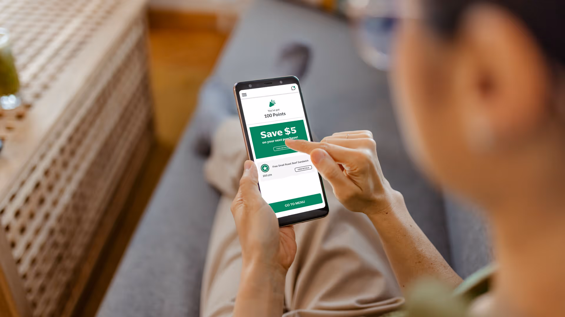 Person holding a smartphone displaying a rewards app with 100 points and a $5 savings offer.