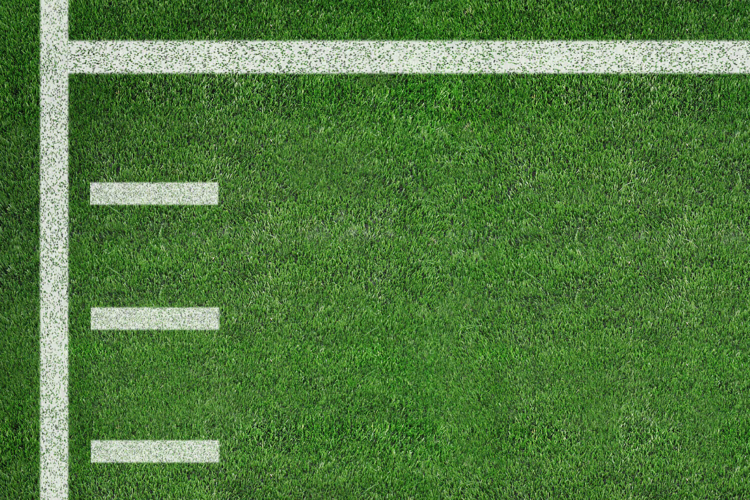 A close-up view of green football field turf with white yard lines and hash marks.