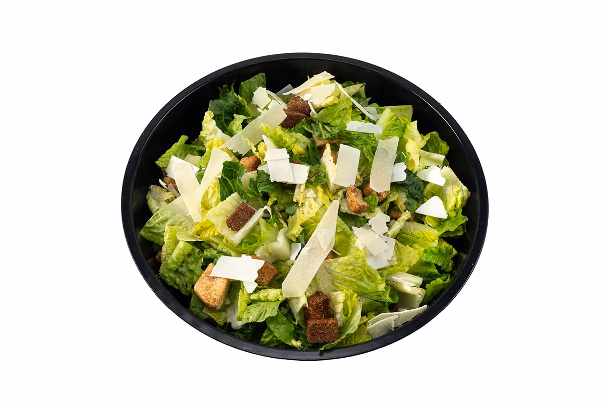 A black bowl filled with Caesar salad, topped with croutons and shaved parmesan cheese, on a white background.