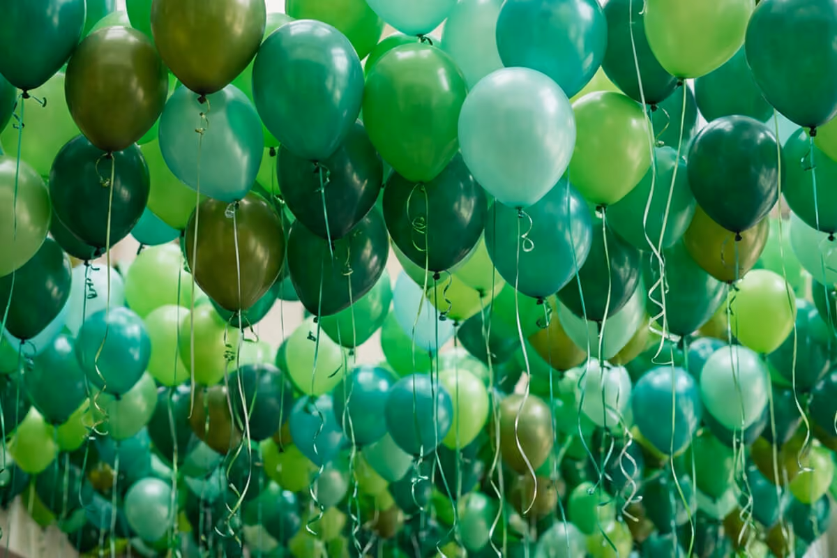 Clusters of helium green balloons in varying shades floating with curled ribbons attached.