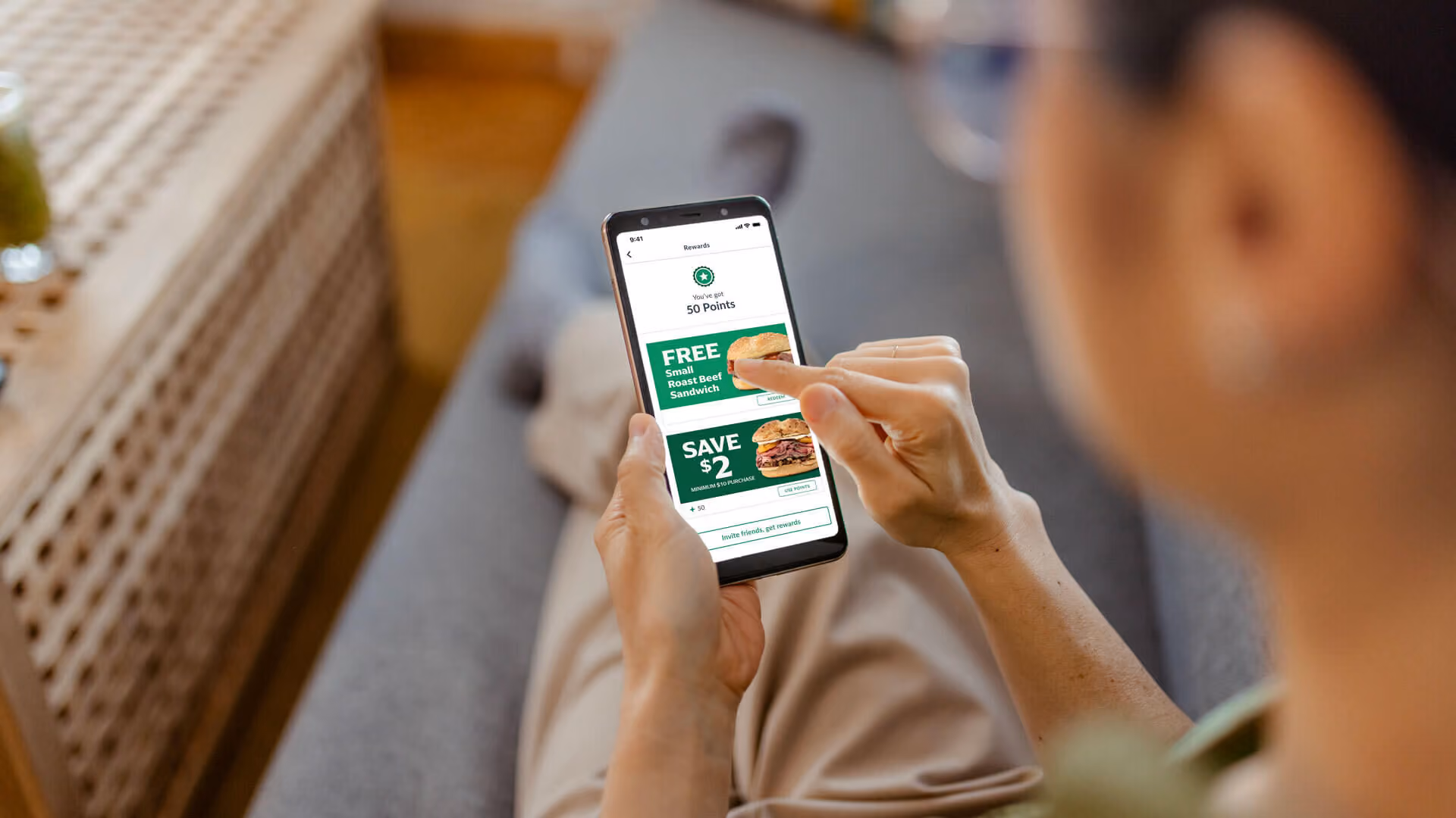 A person uses a smartphone app displaying food rewards for a roast beef sandwich and a two-dollar discount.
