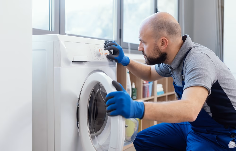 Appliance technician in gloves inspecting front-loading washing machine during home repair