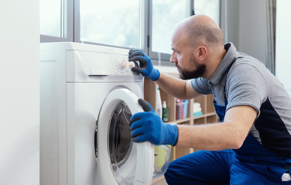 Appliance technician in gloves inspecting front-loading washing machine during home repair