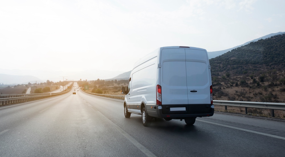 White cargo delivery van driving on open highway through mountainous landscape at sunset