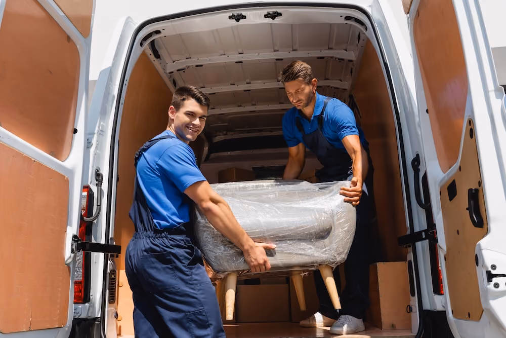 Two professional movers unloading a wrapped sofa from a moving van during a residential move