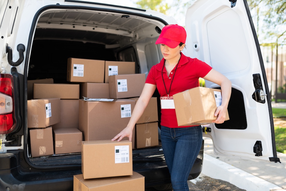 Female courier in red uniform unloading packages from delivery van during last-mile delivery