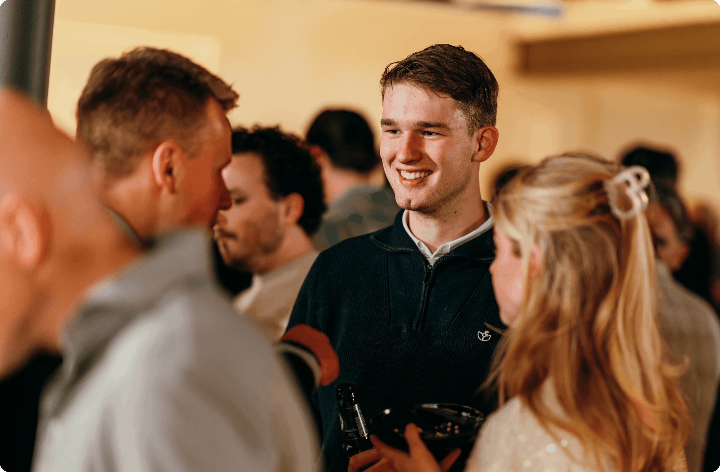 A young man smiling and talking with a group of people at a social gathering.