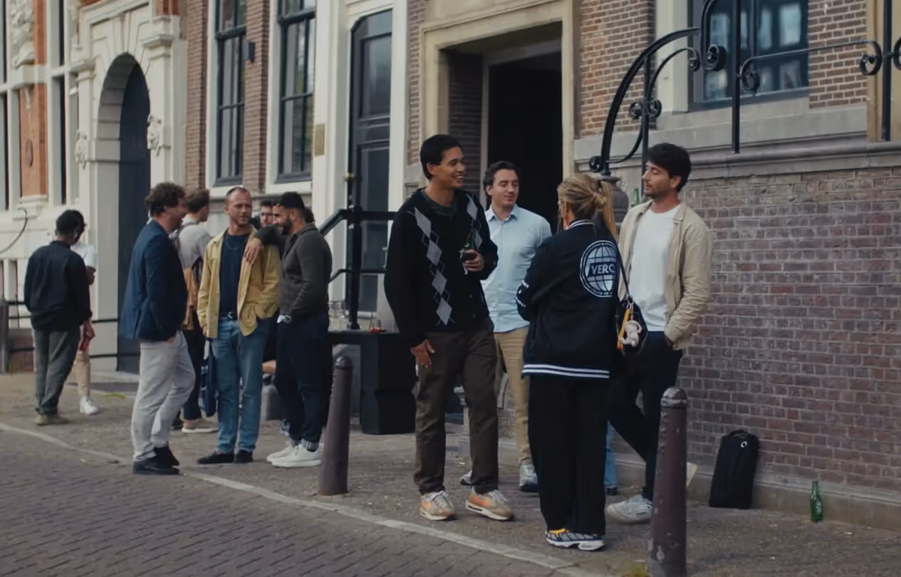 Group of six people casually chatting outdoors, with some holding drinks.