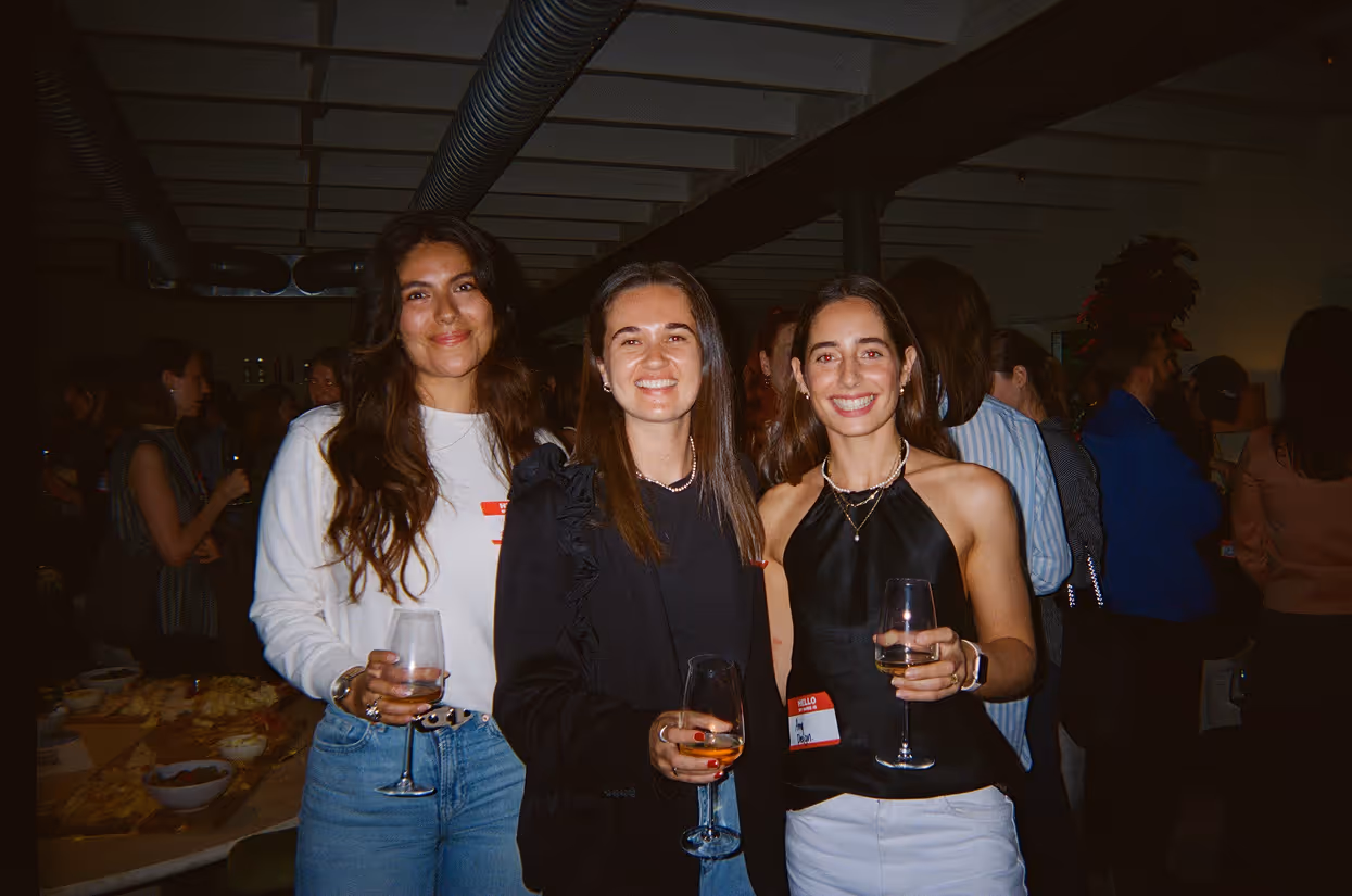 Group of young adults socializing and standing on a cobblestone street beside brick buildings.