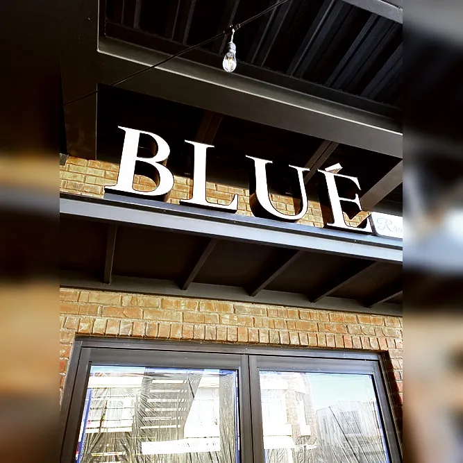 Fotografía de anuncio iluminado 3D con texto "BLUE" con iluminación color blanco neutro instalado sobre fachada comercial