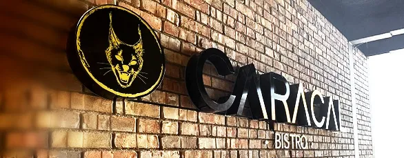 Fotografía de anuncio iluminado 3D con logo y texto "CARACAL" con iluminación color blanco neutro a través de vinil negro y amarillo instalado sobre fachada comercial
