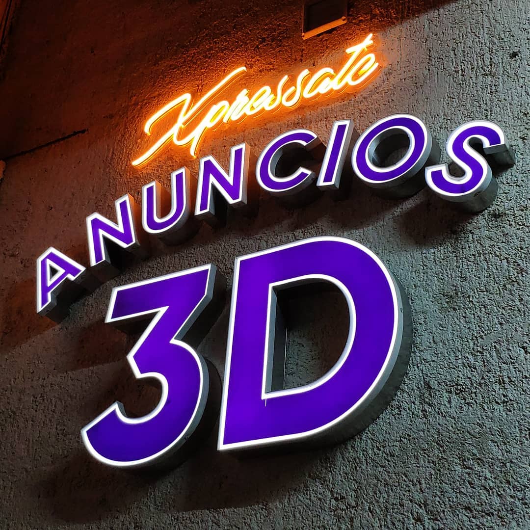Fotografía de anuncio neón LED con texto "Xpressate" color amarillo y anuncio iluminado 3D con texto "ANUNCIOS 3D" con iluminación color blanco neutro a través de acrílico transparente con vinil morado, instalados sobre pared de fachada comercial