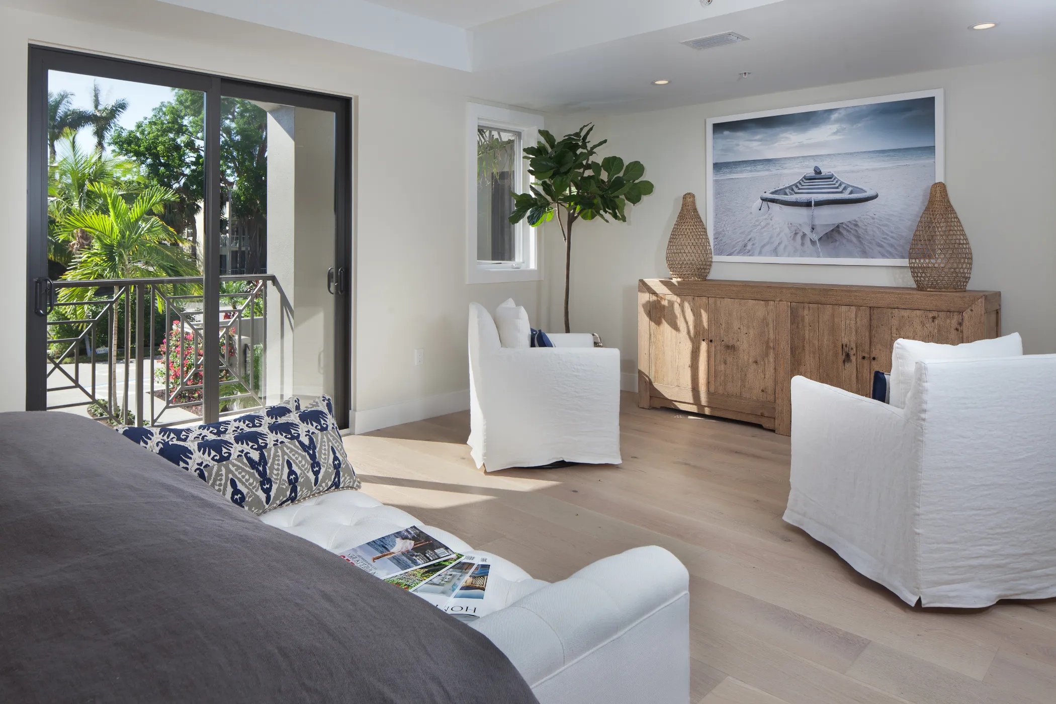 A cozy living room with white armchairs, a wooden cabinet, and a large seascape photo on the wall.