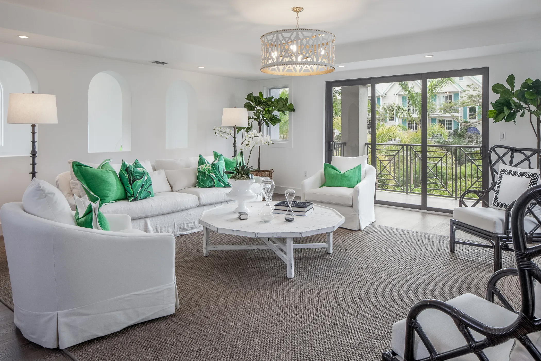 A bright living room with white furniture, green pillows, and large windows overlooking a garden.