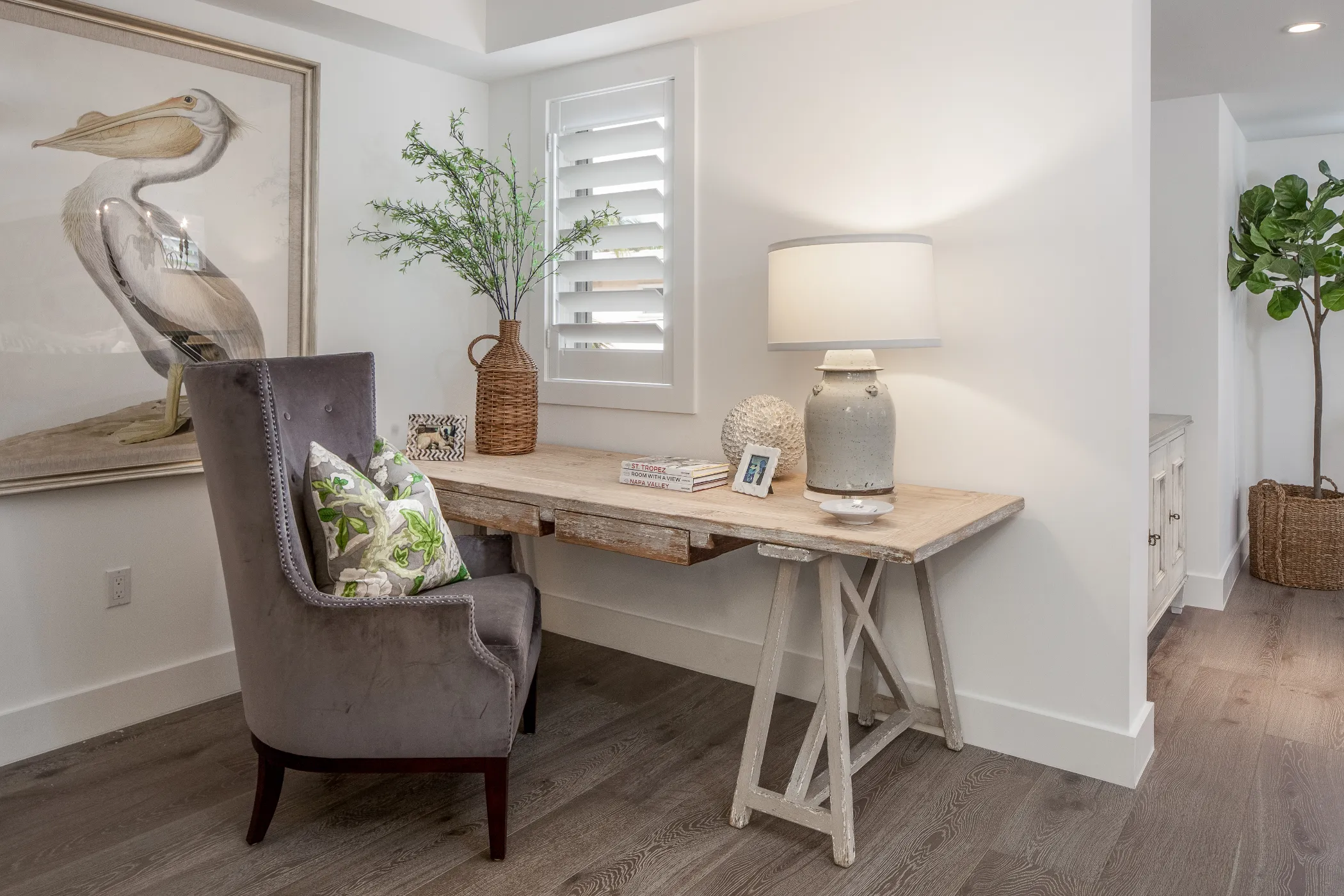A gray chair with cushions sits by a wooden desk with a lamp and decorative items.