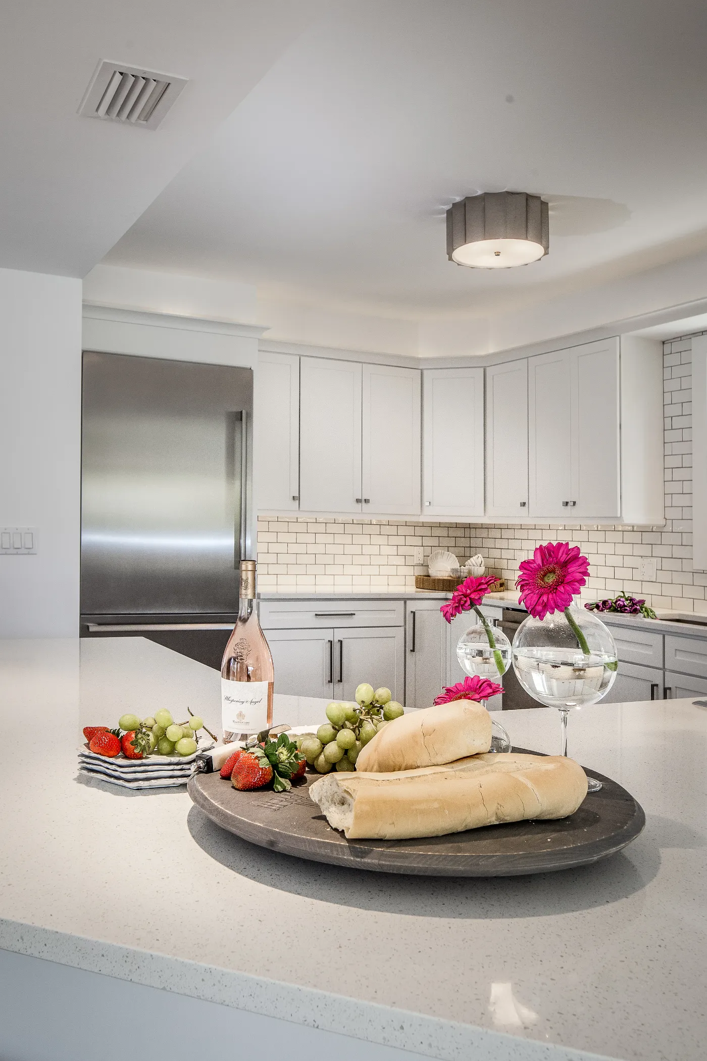 Loaf of bread, grapes, and a bottle of wine on a kitchen counter with flowers nearby.