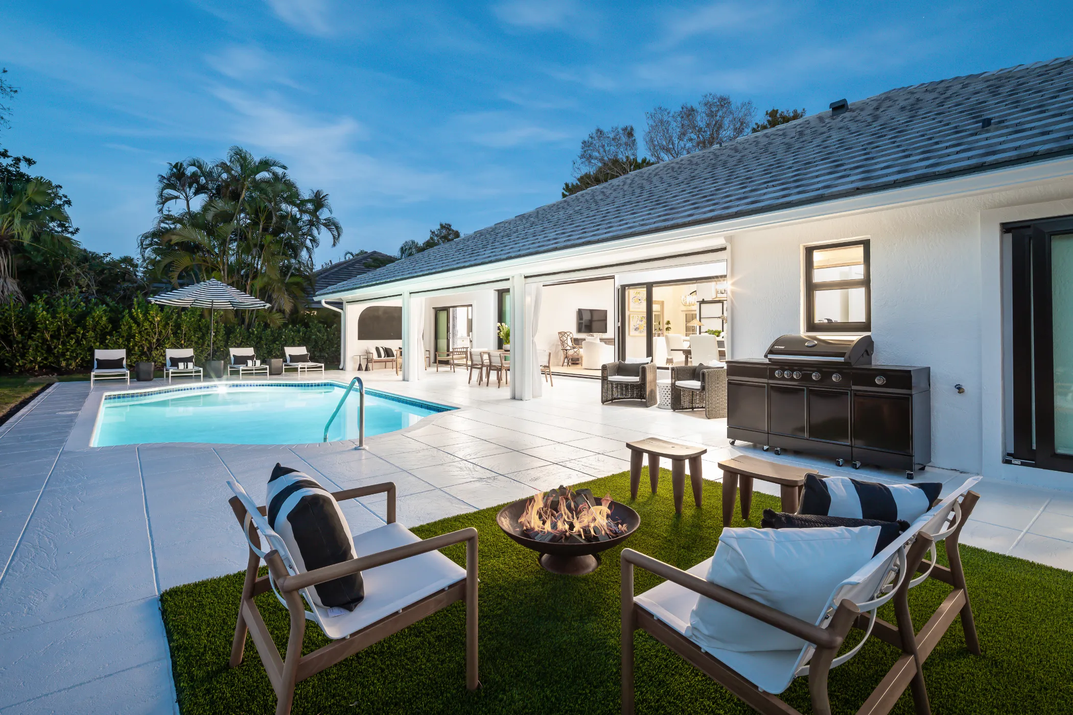 A backyard features a swimming pool, a fire pit, and outdoor seating next to a modern house.