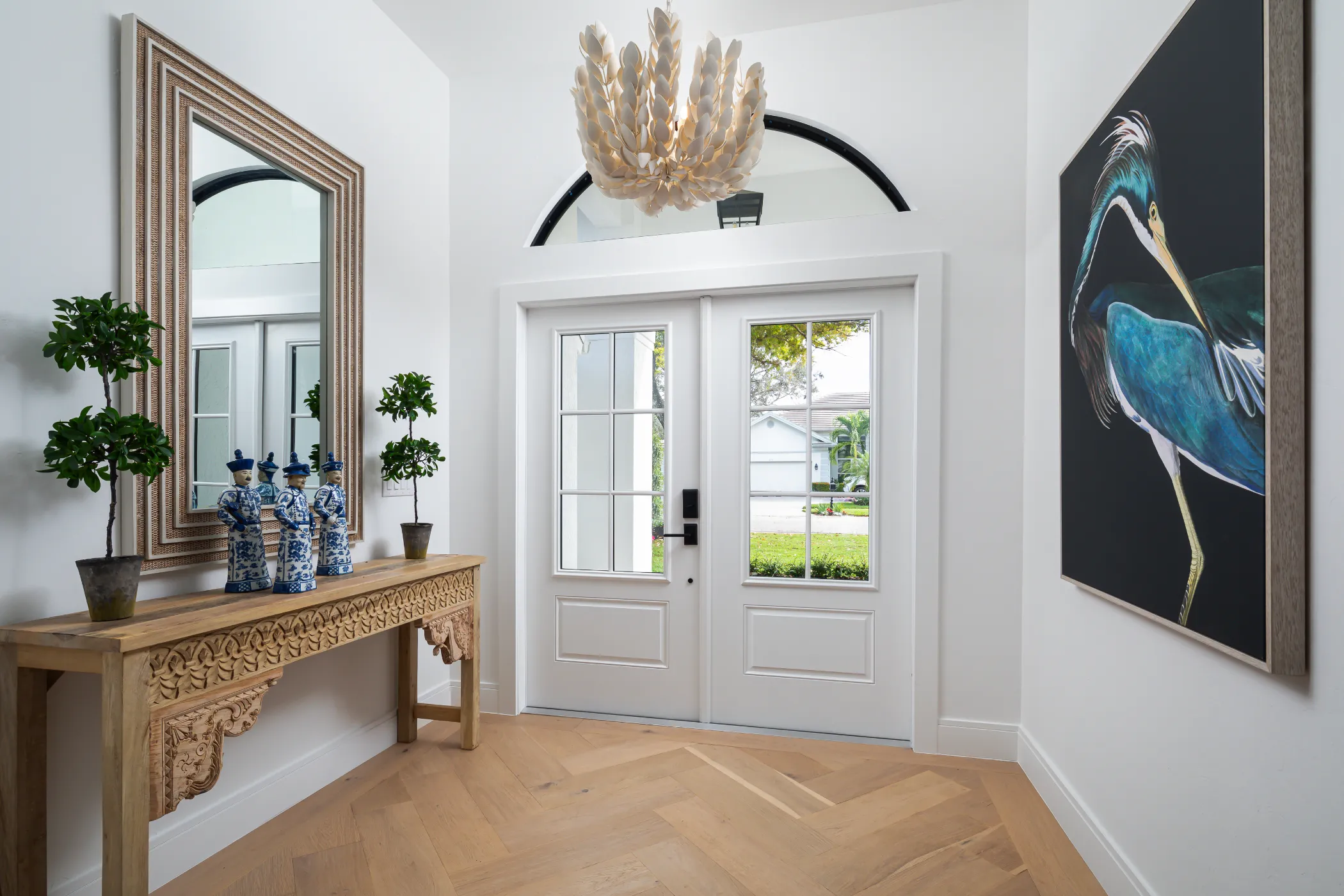A bright entryway with a wooden console table, plants, and a large bird painting on the wall.