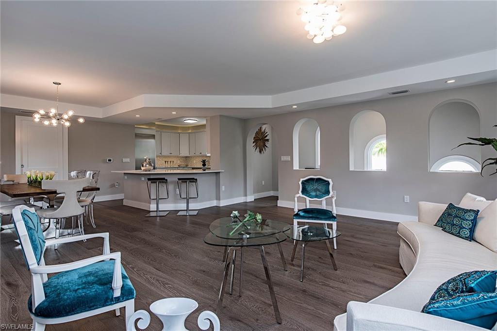 A modern living room with blue chairs, a curved sofa, and a kitchen area in the background.