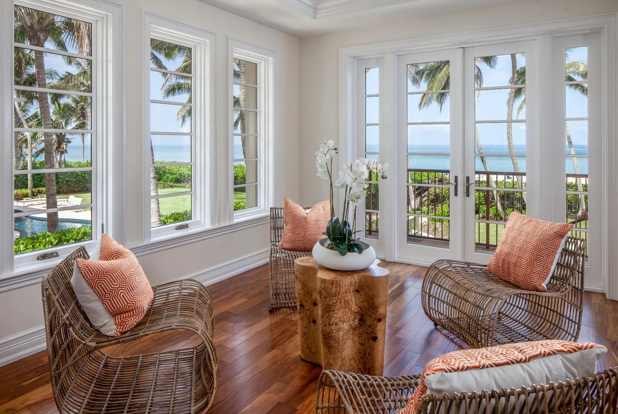 A bright room with wicker chairs, a wooden table, and ocean views through large windows.