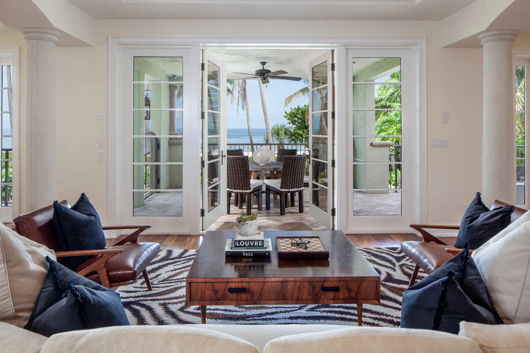 Living room with beige sofas, wooden table, and glass doors opening to a balcony with ocean view.