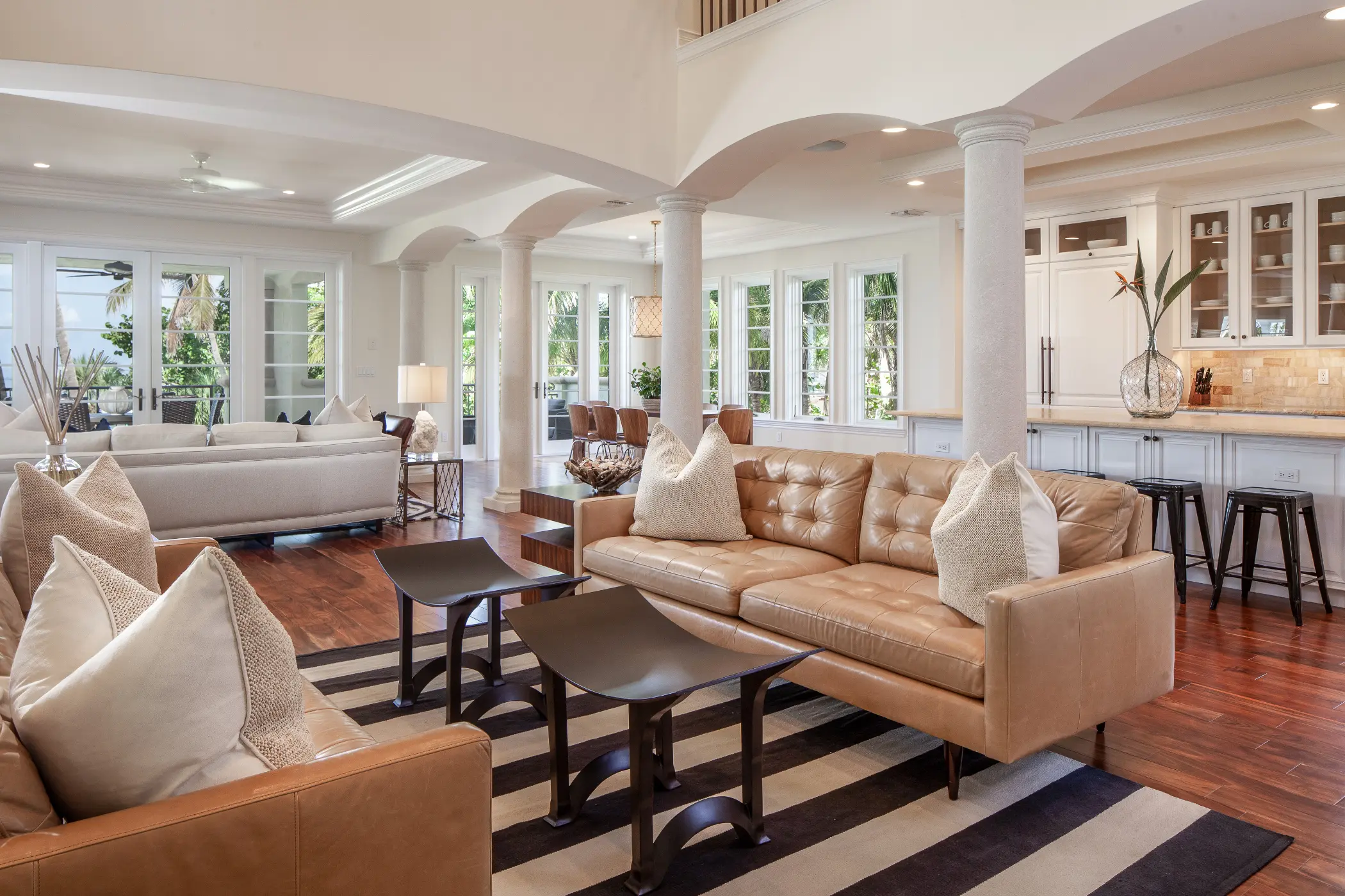 Spacious living room with brown leather sofas, dark wood tables, and a view of the kitchen.