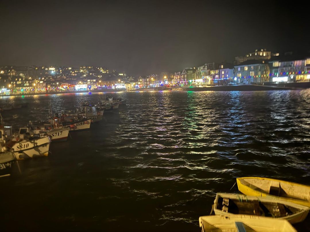 St Ives harbour lit up at night at Christmas, with fishing boats in the foreground