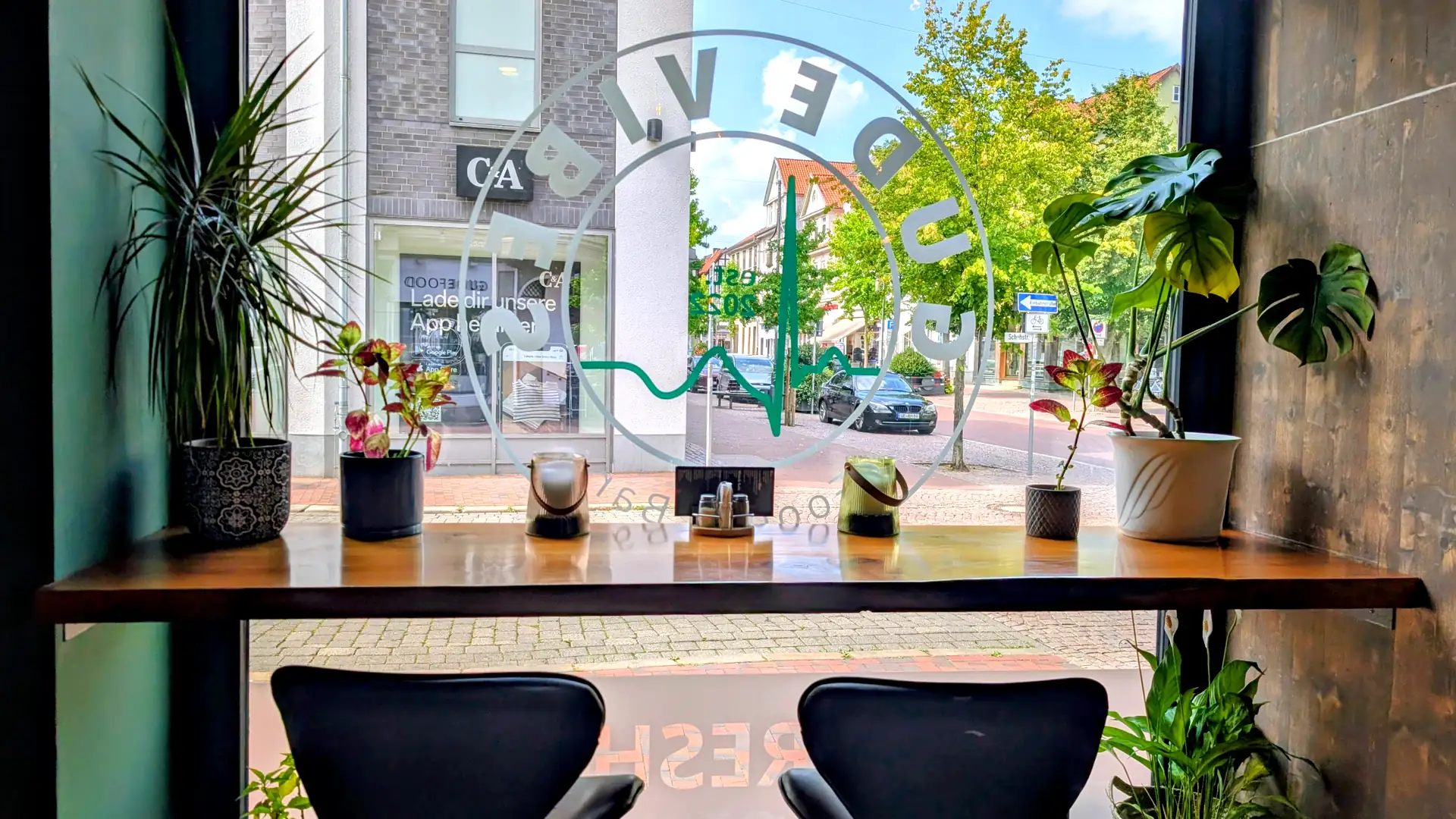 Fensterplatz im Gude Vibes Uelzen mit Pflanzen und Blick durch das Logo auf die Gudesstraße