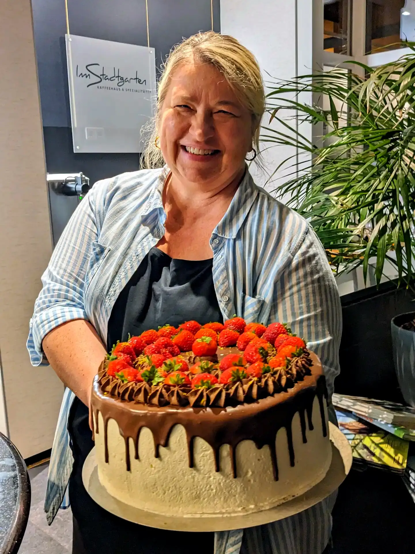 Inhaberin Mira mit einer Erdbeer-Schoko-Torte vor dem Schild vom Im Stadtgarten Uelzen