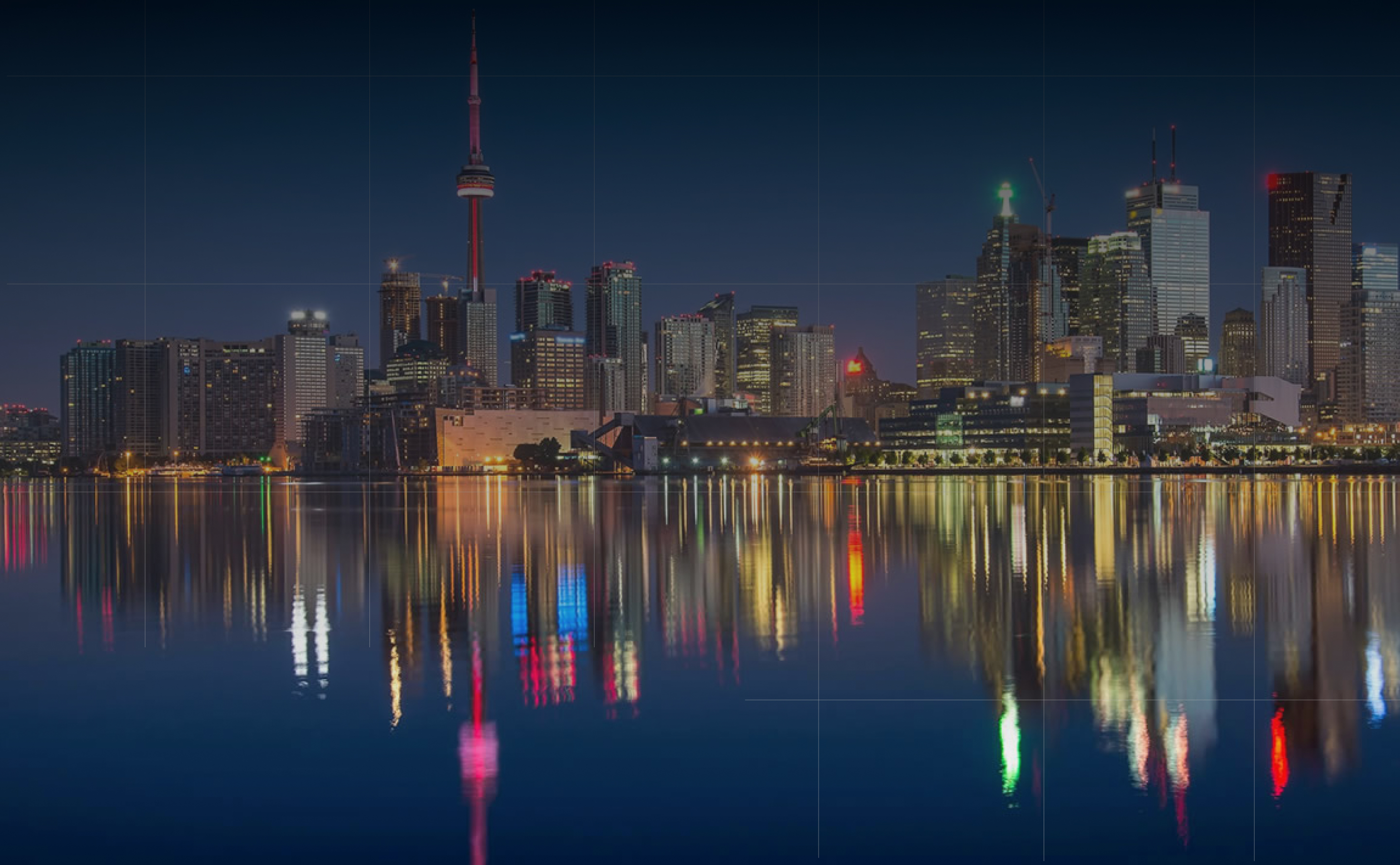 Toronto skyline at night with illuminated buildings and CN Tower reflected in calm water.