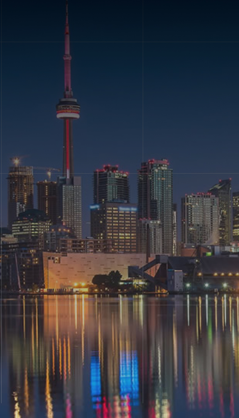 Night view of Toronto skyline with CN Tower and building lights reflecting on water.