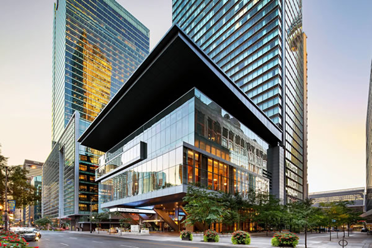 Modern glass and steel high-rise buildings at a city street intersection at dusk with lights on.