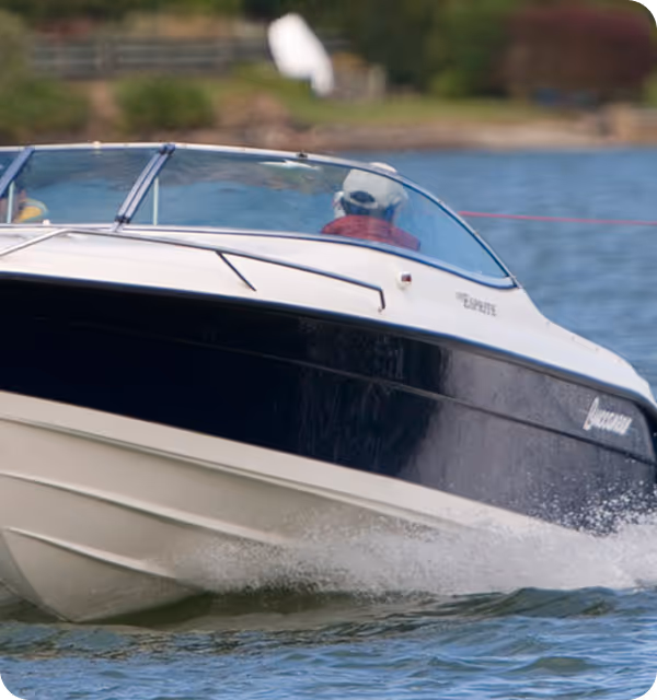 A person wearing a cap driving a black and white speedboat on a lake.