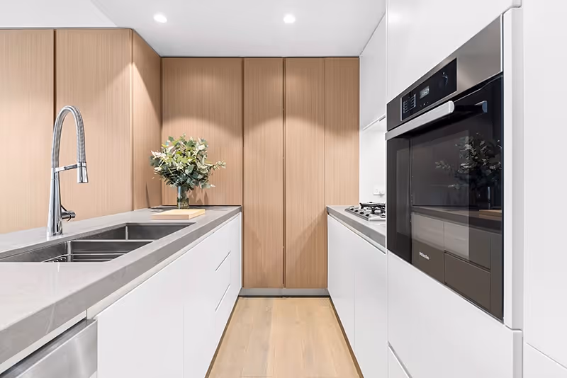 Photo of an apartment kitchen with timber look cupboards, sink, benches and oven