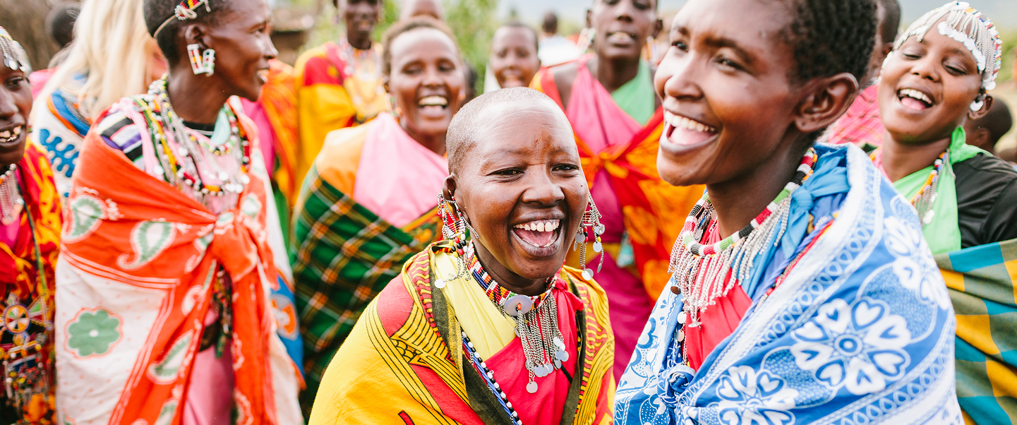 Group of Maasai people in colorful traditional attire smiling together in the Maasai Mara.