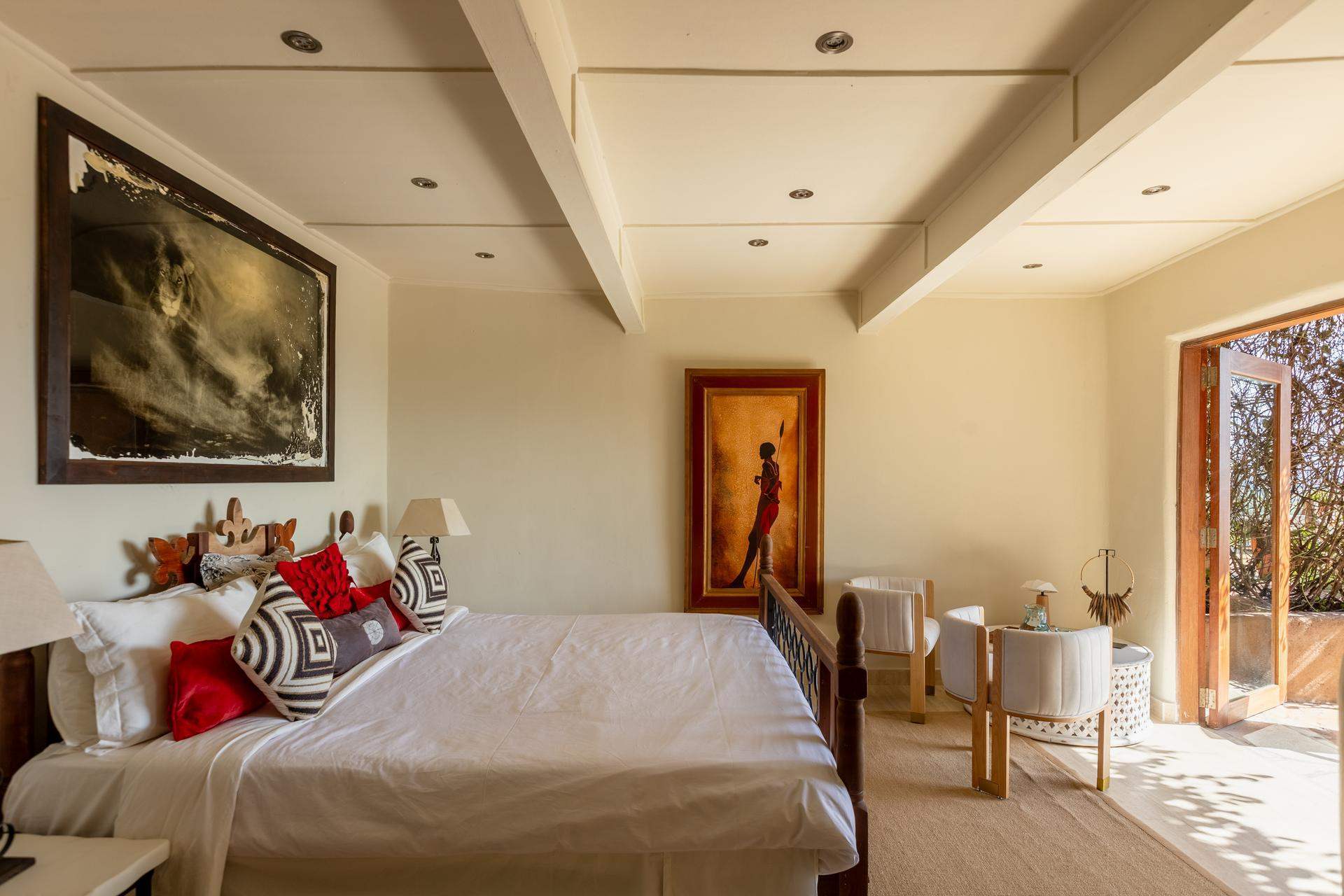Framed Maasai artwork above a soft-toned bed with natural light from a veranda door.
