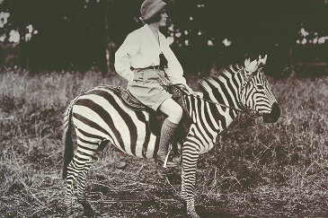 Historic image of safari guests and guides in traditional attire beside early touring vehicles in Kenya.