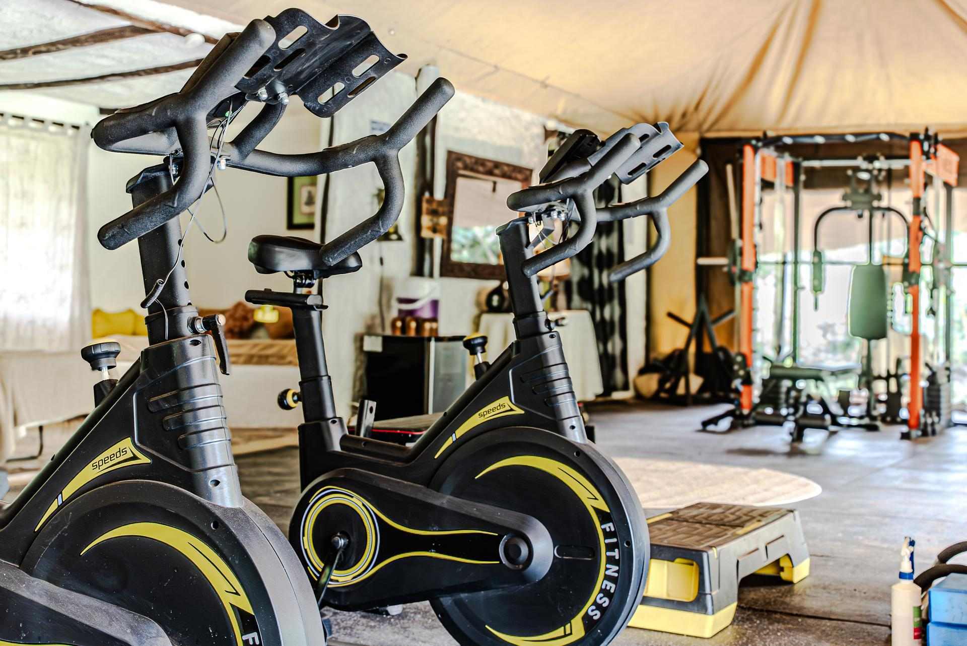 Gym in a Tent Cottar’s 1920s Camp gym tent featuring modern fitness equipment including spin bikes and weight machines within a canvas structure.