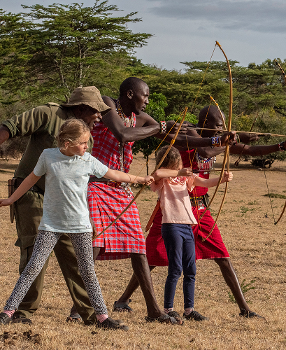 Maasai warriors teaching children traditional archery skills in the bush.