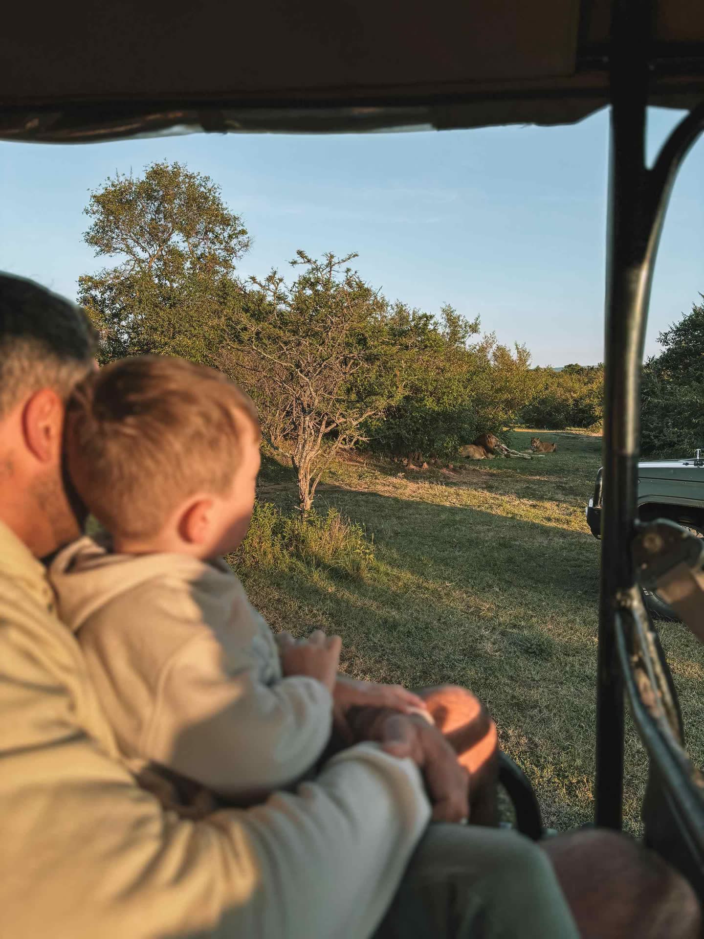 Parent and child watching lions during a guided safari in Kenya’s Maasai Mara.