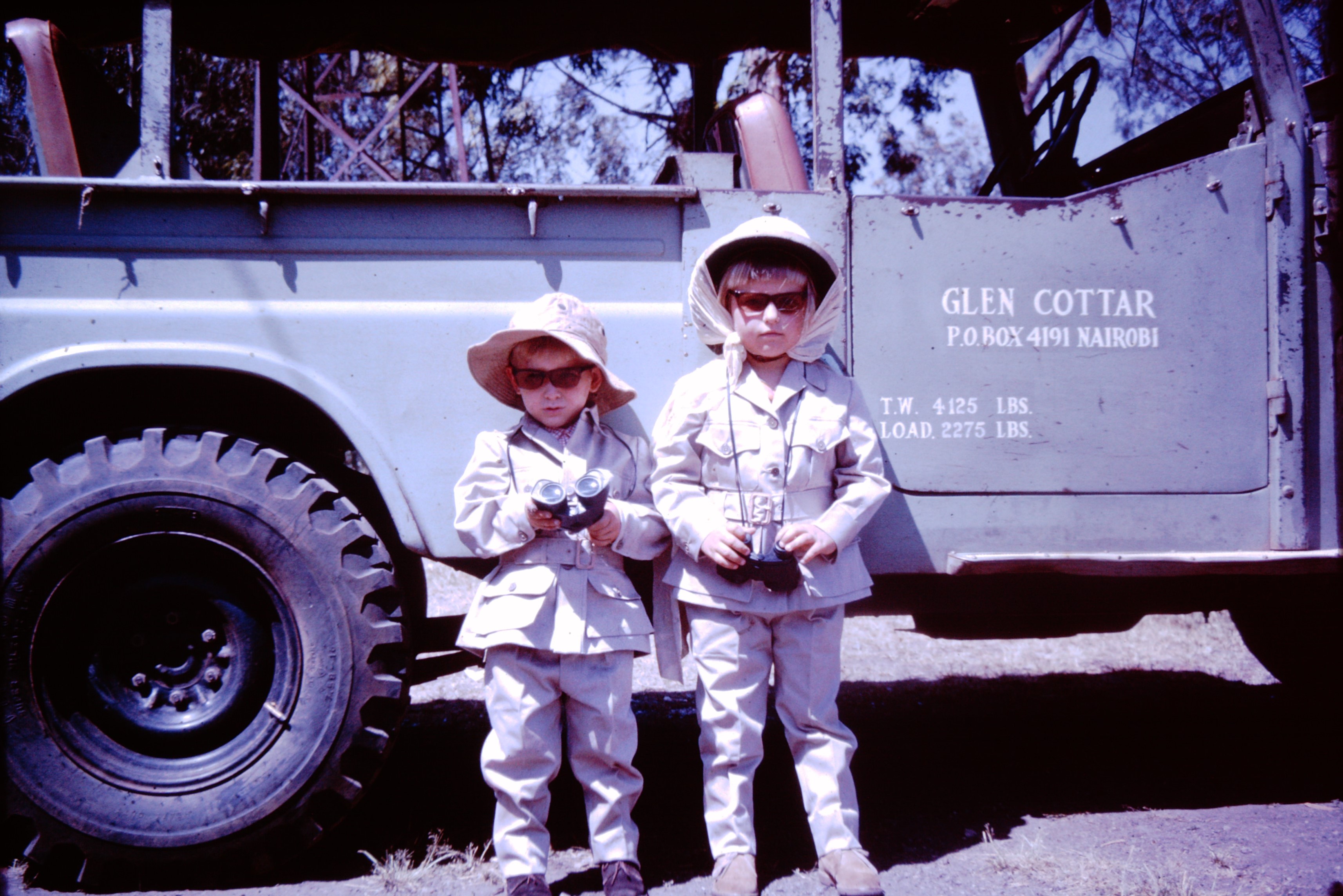 Young Calvin Cottar and his sibling standing beside a family safari vehicle with binoculars in Kenya.