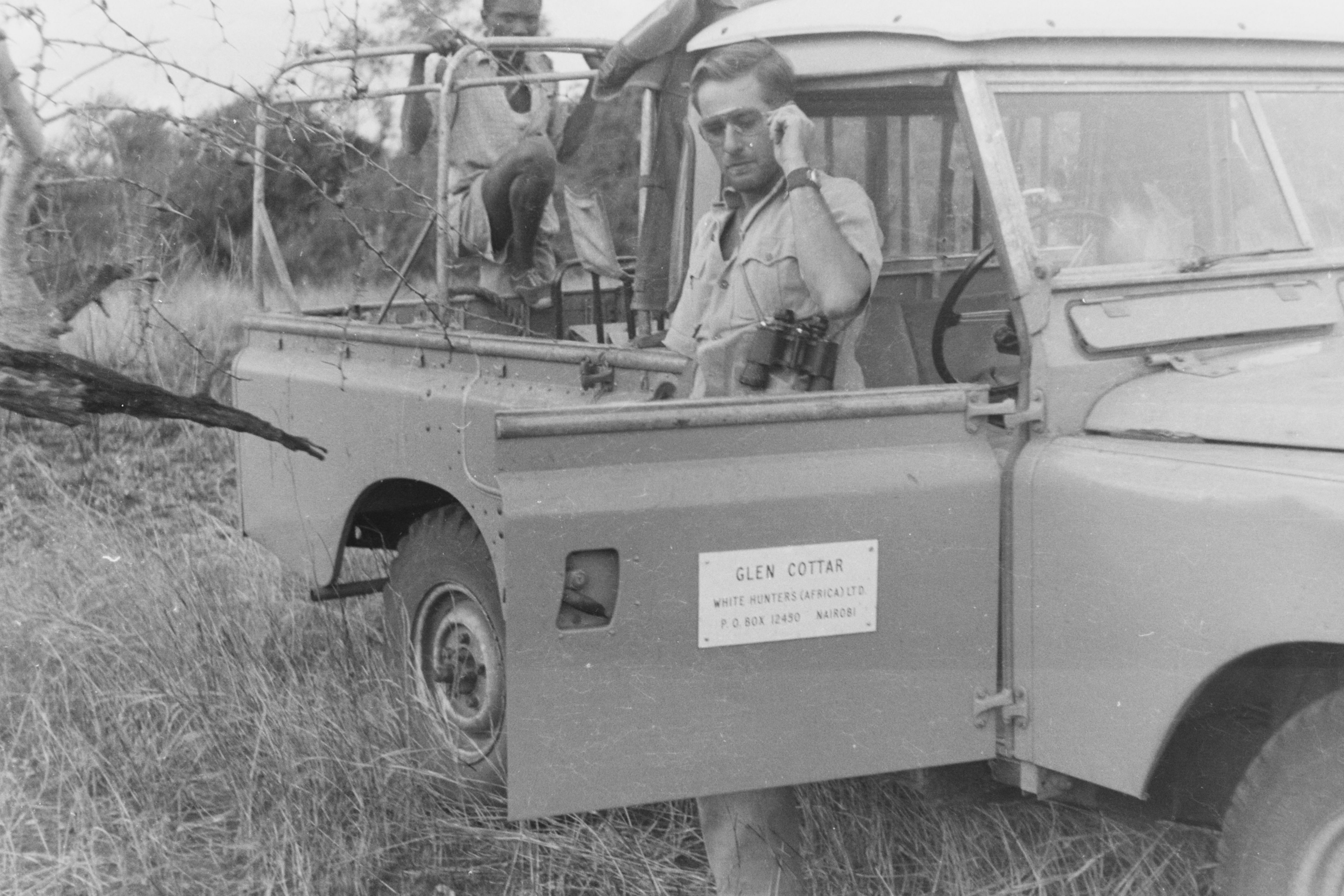 Historic photograph of Glen Cottar beside an early safari vehicle during a wildlife expedition in Kenya.