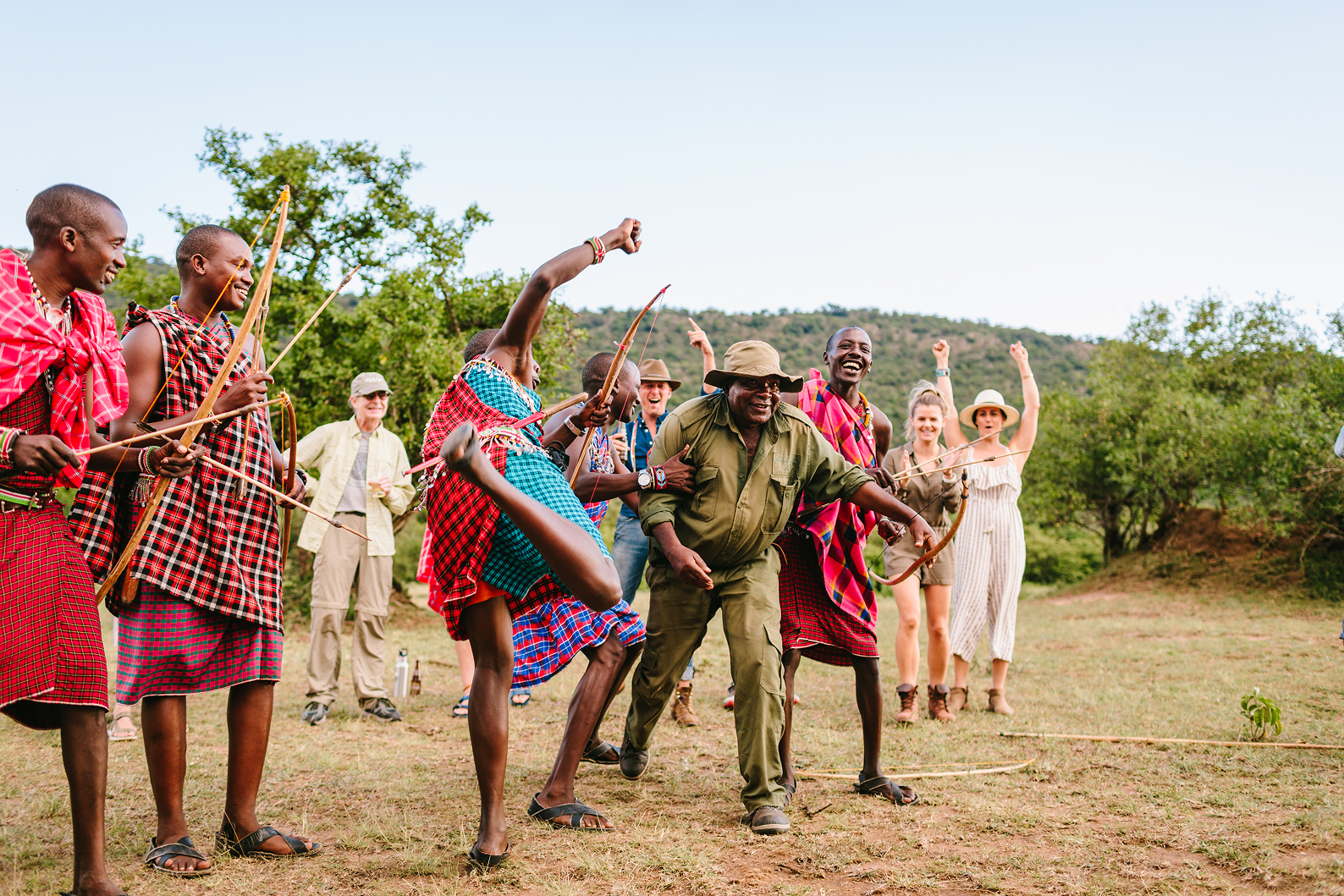 Guests and Maasai guides celebrating after a traditional archery activity during a family safari.
