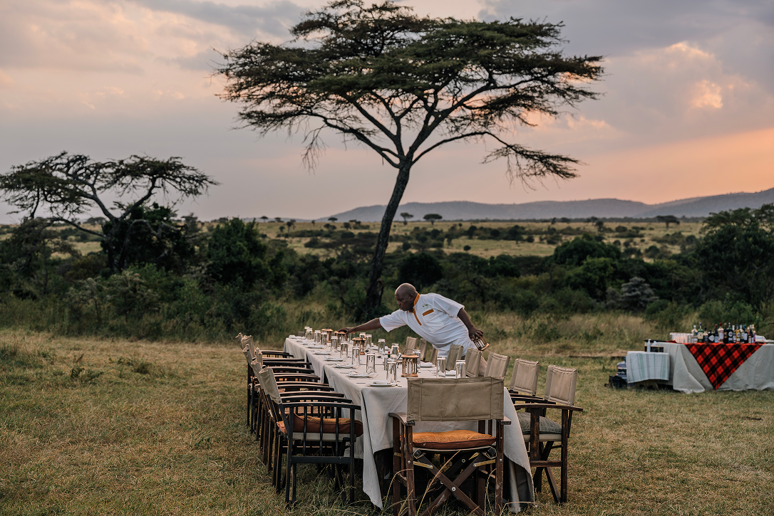 Camp staff preparing an outdoor bush dinner in the Maasai Mara at sunset.